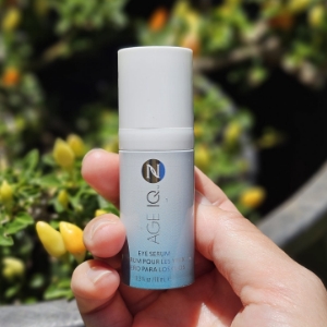 Hand holding eye serum in front of a plant